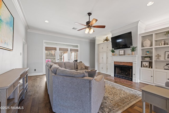 living room featuring visible vents, a tiled fireplace, ornamental molding, a ceiling fan, and dark wood-style flooring