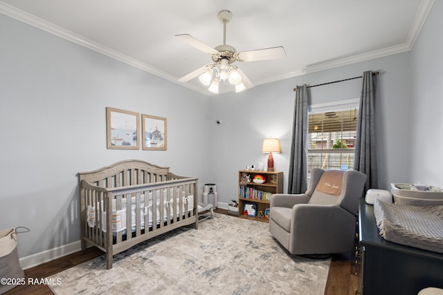 bedroom with a nursery area, ornamental molding, baseboards, and wood finished floors