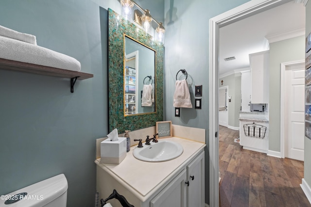 half bath featuring vanity, toilet, wood finished floors, and ornamental molding