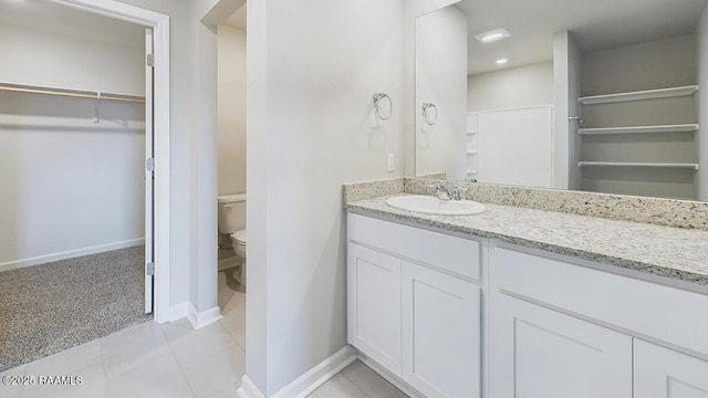 full bathroom featuring vanity, baseboards, a spacious closet, tile patterned floors, and toilet