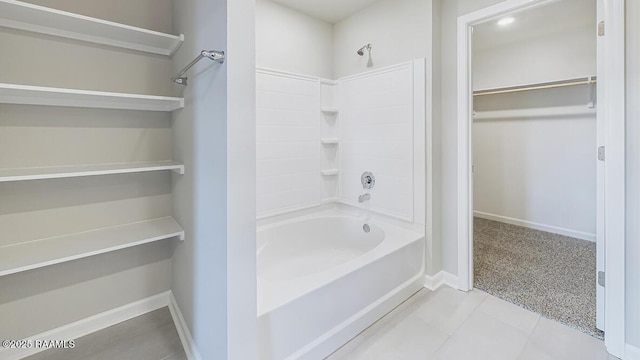 bathroom with tile patterned floors, a spacious closet, washtub / shower combination, and baseboards