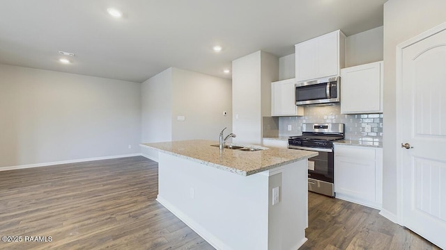 kitchen featuring a kitchen island with sink, a sink, dark wood-style floors, appliances with stainless steel finishes, and decorative backsplash