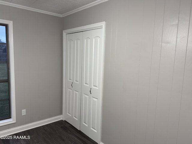 unfurnished bedroom with a closet, ornamental molding, baseboards, and dark wood-style flooring