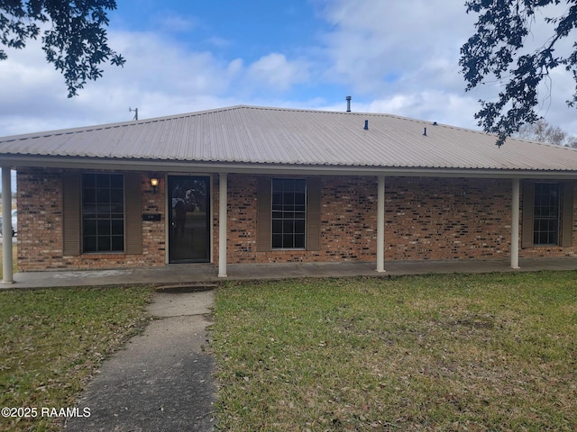 view of front facade with a front yard, a porch, brick siding, and metal roof