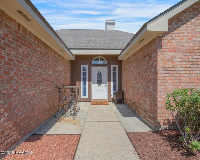 doorway to property with brick siding, a chimney, and a shingled roof