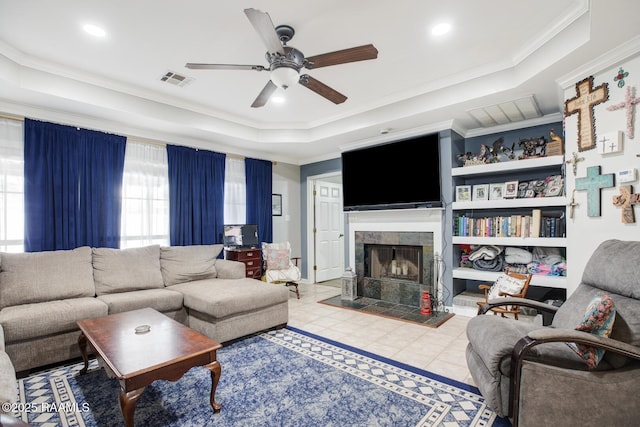 tiled living room featuring a ceiling fan, visible vents, a tray ceiling, a fireplace, and crown molding