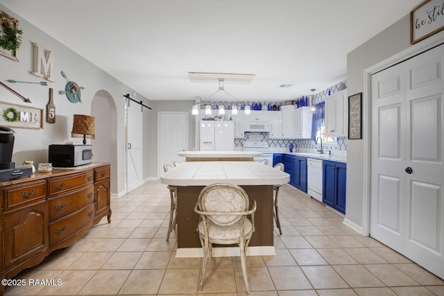 kitchen featuring a center island, tile counters, a barn door, white appliances, and blue cabinets