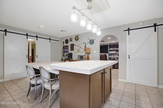 kitchen with light tile patterned floors, a barn door, arched walkways, and a kitchen island