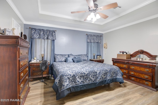 bedroom with a ceiling fan, a tray ceiling, light wood-style floors, and visible vents