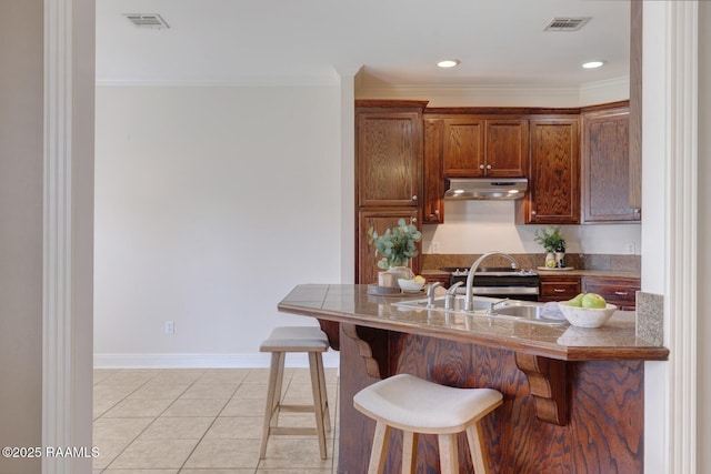 kitchen with under cabinet range hood, visible vents, a kitchen breakfast bar, and light tile patterned flooring