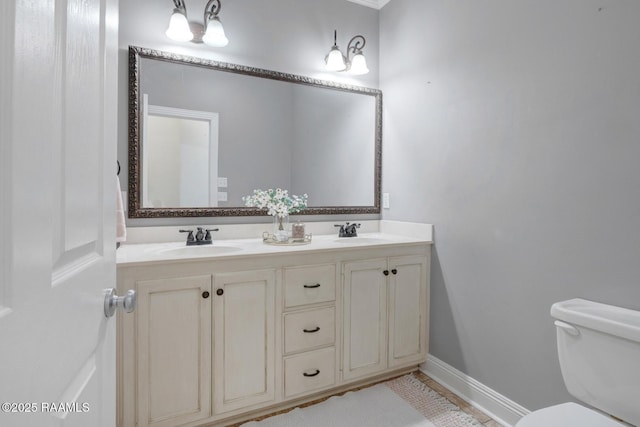 bathroom featuring double vanity, toilet, baseboards, and a sink