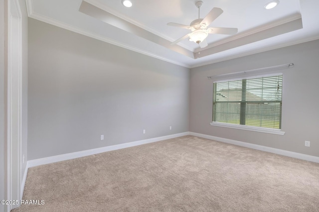 carpeted empty room featuring a ceiling fan, a raised ceiling, baseboards, and ornamental molding