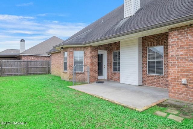 back of house with fence, roof with shingles, a lawn, a patio area, and brick siding