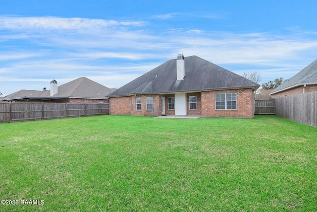 rear view of property featuring a patio, a fenced backyard, a yard, brick siding, and a chimney