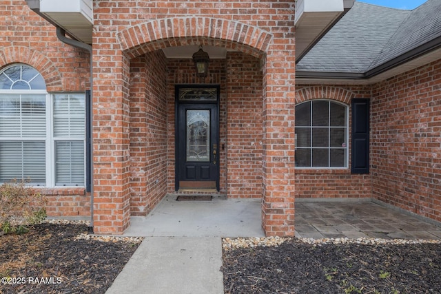 view of exterior entry with brick siding and roof with shingles