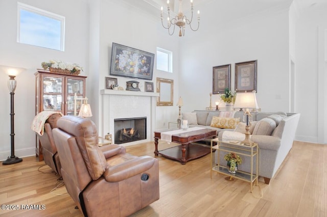 living area featuring a towering ceiling, light wood-style floors, a fireplace, baseboards, and a chandelier