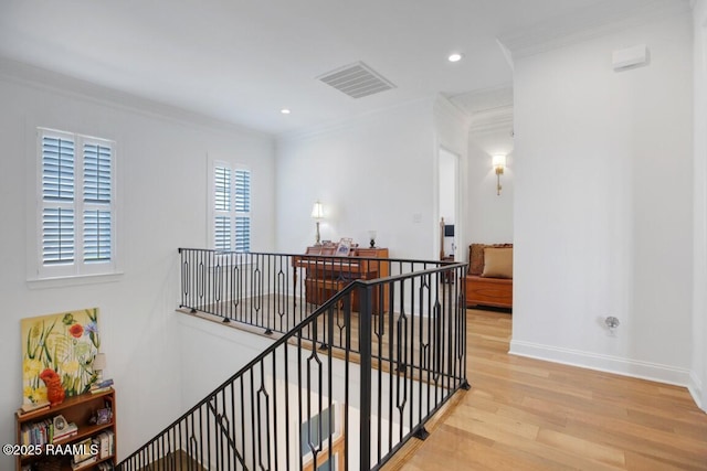 hall with baseboards, visible vents, light wood-style flooring, ornamental molding, and an upstairs landing