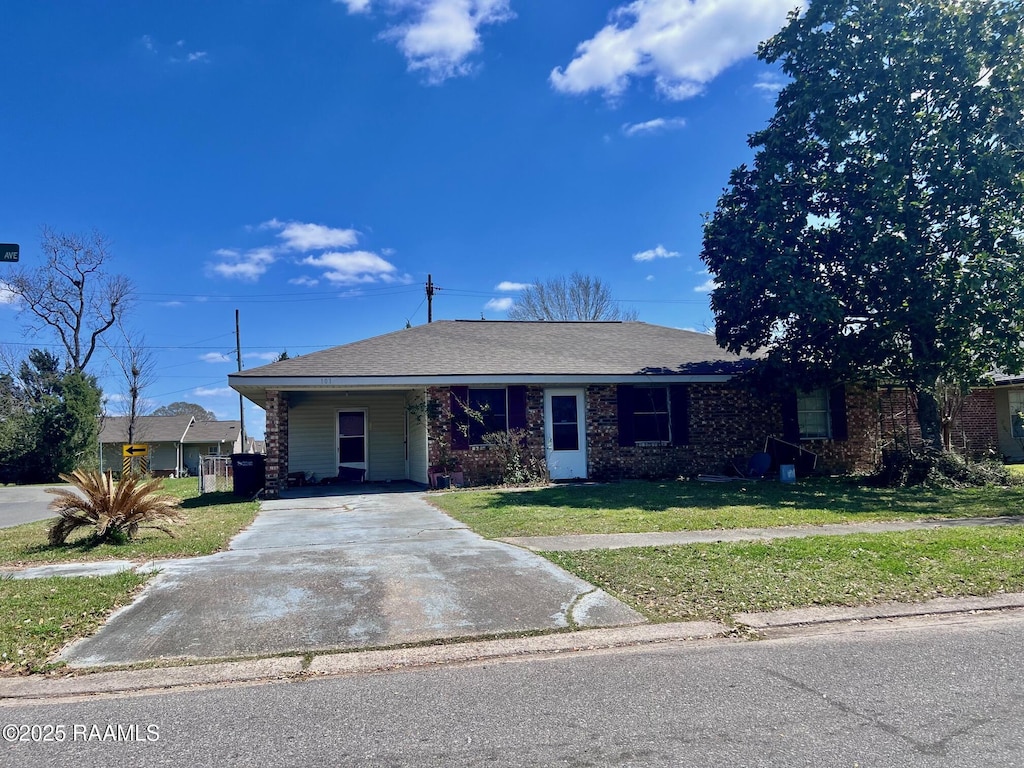 single story home featuring a front lawn, an attached carport, roof with shingles, concrete driveway, and brick siding