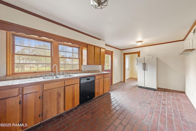 kitchen with a sink, freestanding refrigerator, tile countertops, brick floor, and dishwasher