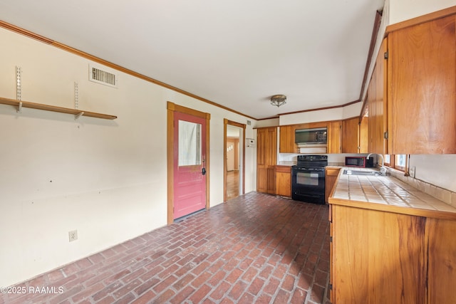 kitchen featuring visible vents, black range with electric stovetop, tile countertops, brick floor, and a sink