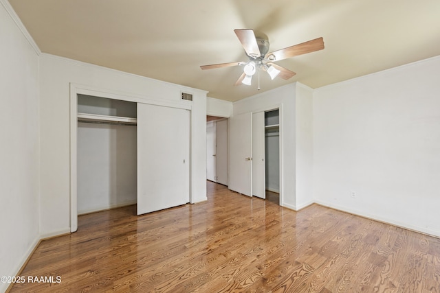 unfurnished bedroom featuring wood finished floors, baseboards, visible vents, multiple closets, and crown molding