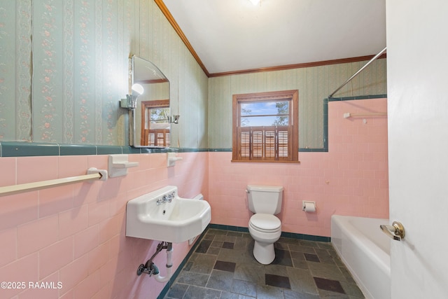 bathroom featuring wallpapered walls, toilet, a sink, and wainscoting