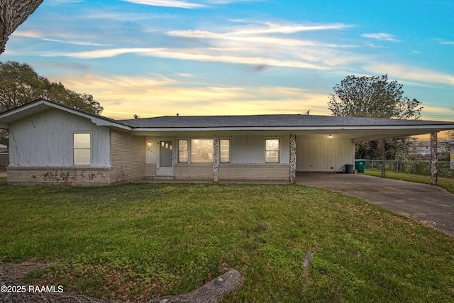 ranch-style house with brick siding, an attached carport, a shingled roof, concrete driveway, and a lawn