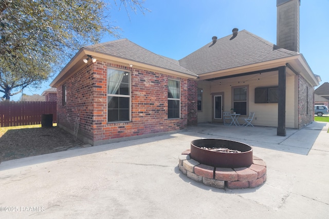 back of house with brick siding, a fire pit, fence, roof with shingles, and a patio area