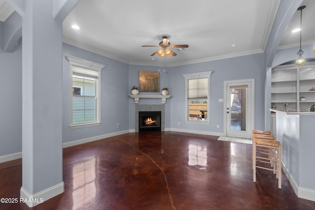 unfurnished living room with a warm lit fireplace, concrete floors, crown molding, baseboards, and ceiling fan