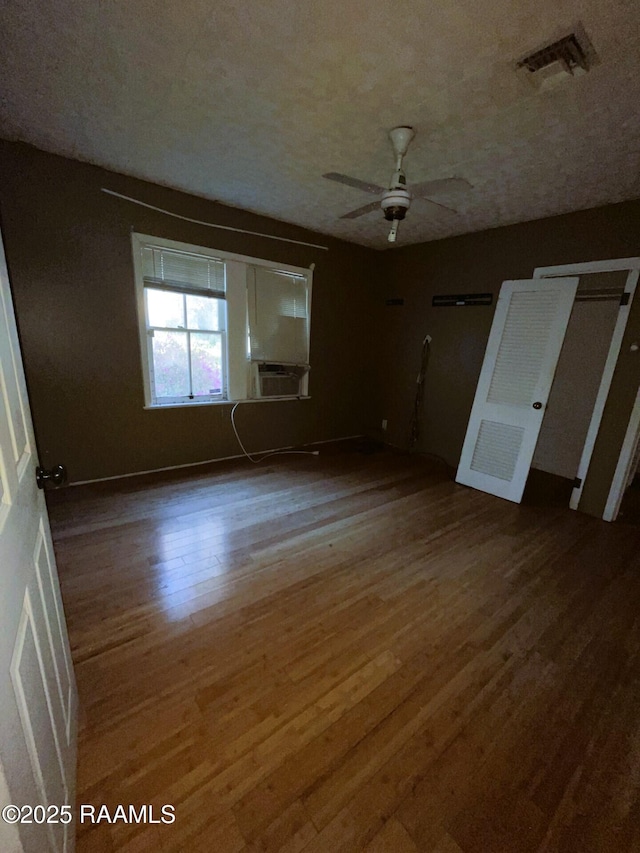 unfurnished bedroom featuring cooling unit, wood finished floors, visible vents, ceiling fan, and a textured ceiling