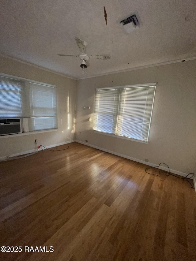 empty room featuring cooling unit, wood finished floors, baseboards, visible vents, and ornamental molding