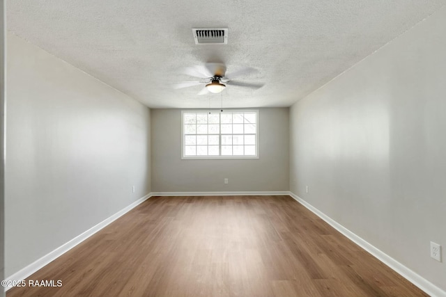 spare room featuring wood finished floors, baseboards, visible vents, ceiling fan, and a textured ceiling