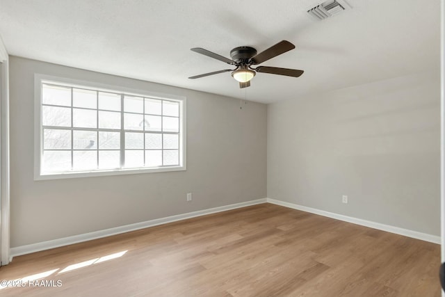 spare room featuring a ceiling fan, visible vents, light wood-style floors, and baseboards