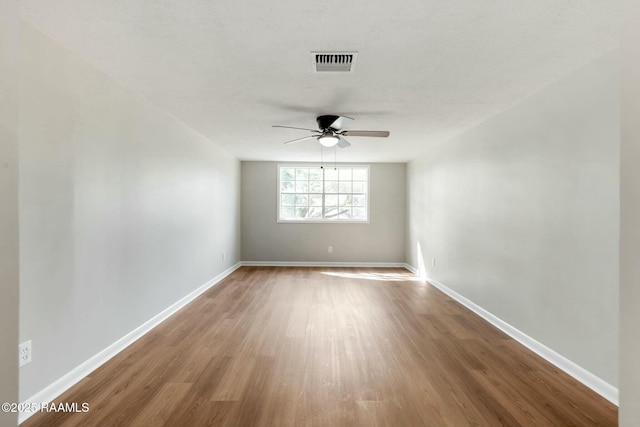 spare room featuring visible vents, wood finished floors, baseboards, and ceiling fan