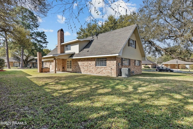 rear view of property with brick siding, a shingled roof, central air condition unit, a chimney, and a yard