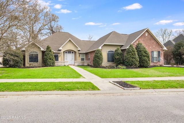 view of front facade featuring stucco siding, brick siding, roof with shingles, and a front yard