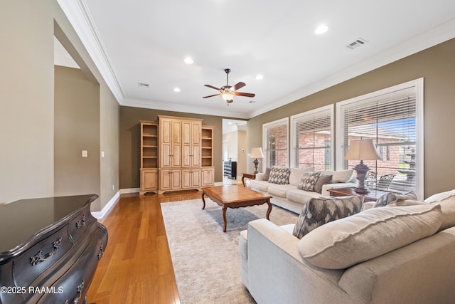 living room featuring light wood-style flooring, baseboards, visible vents, ceiling fan, and ornamental molding