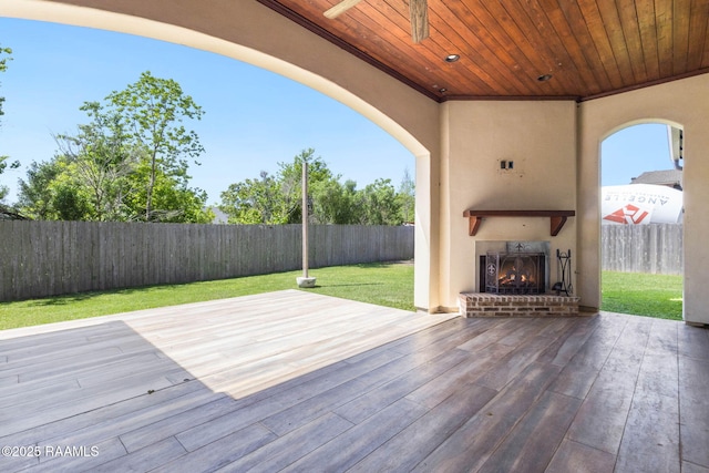 wooden terrace with an outdoor brick fireplace, a fenced backyard, and a lawn