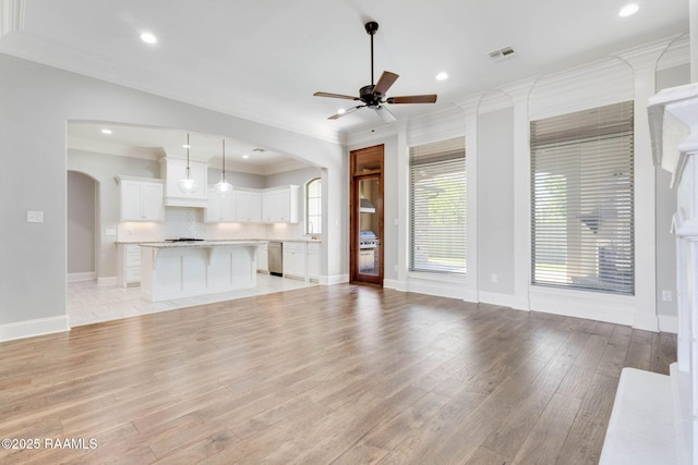 unfurnished living room featuring light wood finished floors, arched walkways, visible vents, ceiling fan, and crown molding