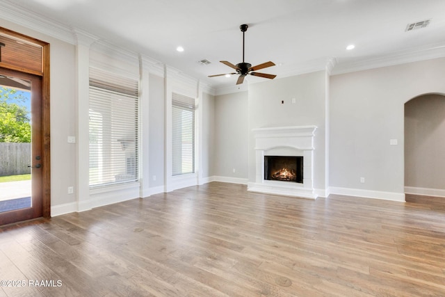 unfurnished living room featuring light wood finished floors, visible vents, ornamental molding, arched walkways, and ceiling fan