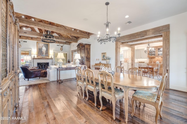 dining area with visible vents, beam ceiling, a fireplace, an inviting chandelier, and hardwood / wood-style flooring