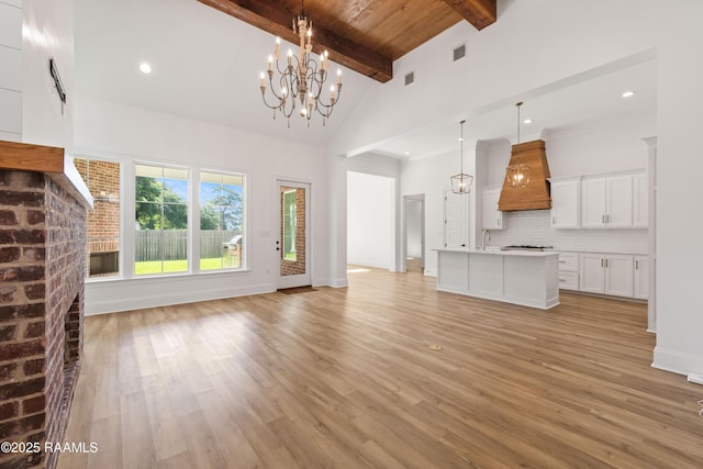 303 Canary Palm Way, Youngsville, LA 70592 - unfurnished living room with a chandelier, beam ceiling, light wood-style flooring, high vaulted ceiling, and a brick fireplace
