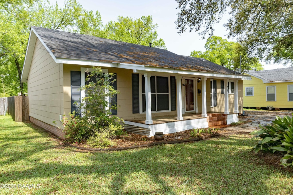 view of front facade with covered porch, a shingled roof, and a front lawn