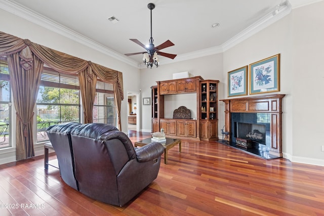 living room featuring visible vents, ornamental molding, wood finished floors, a fireplace, and ceiling fan
