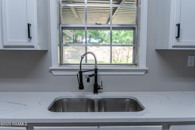 kitchen with a sink, light stone counters, and white cabinetry