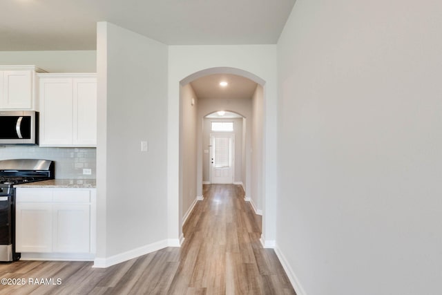 hallway featuring arched walkways, light wood finished floors, and baseboards