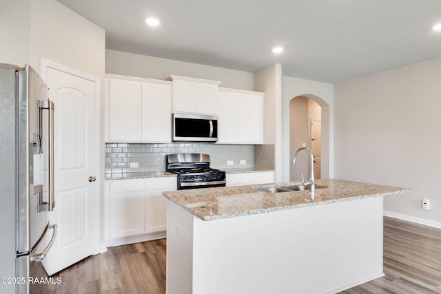 kitchen with a sink, a center island with sink, decorative backsplash, light wood-style flooring, and appliances with stainless steel finishes