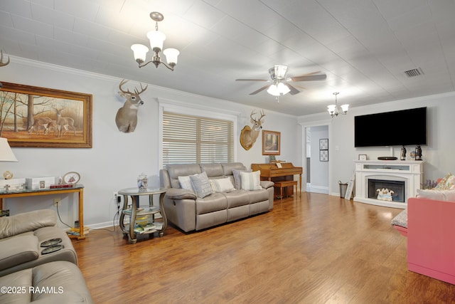 living room featuring ornamental molding, ceiling fan with notable chandelier, baseboards, and wood finished floors
