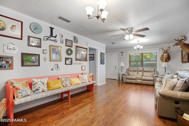living room featuring ornamental molding, ceiling fan with notable chandelier, baseboards, visible vents, and wood finished floors