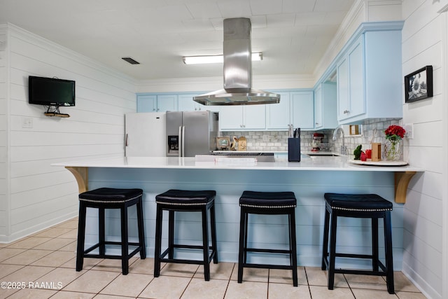 kitchen featuring blue cabinetry, stainless steel fridge, island range hood, decorative backsplash, and a peninsula